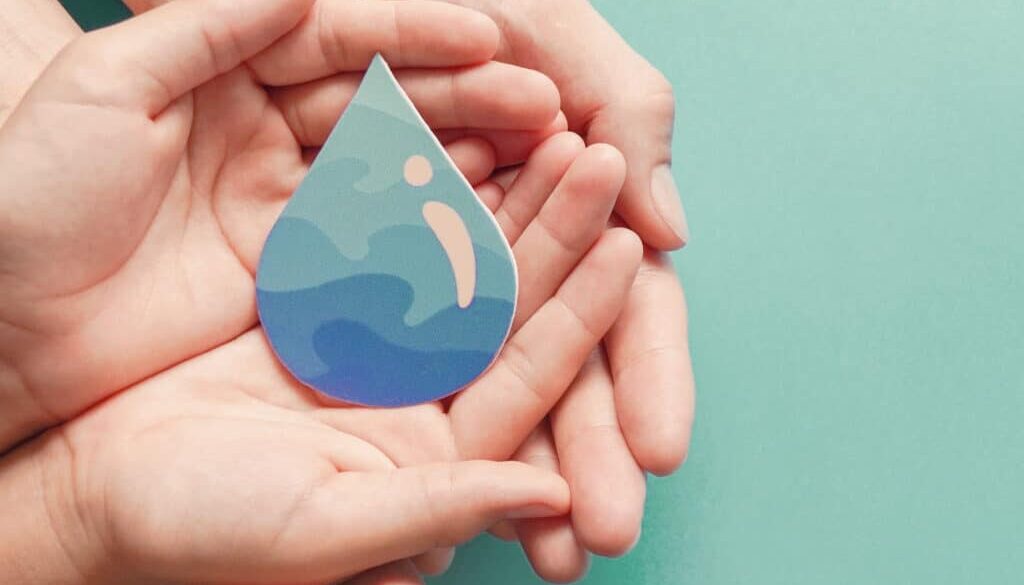 Deux paires de mains ouvertes tiennent une goutte d'eau en papier avec un motif abstrait bleu et vert, représentant des vagues. L'arrière-plan est d'une couleur vert pâle unie.