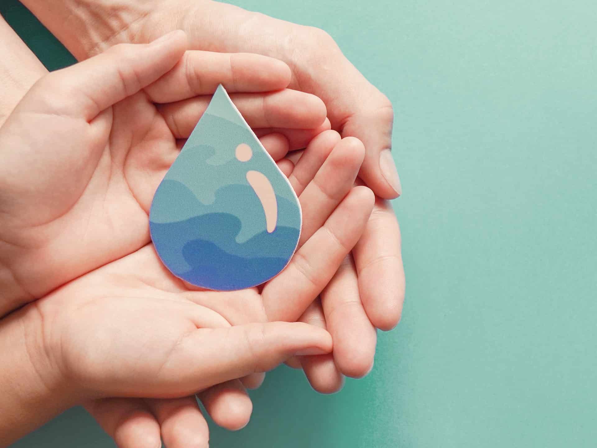 Deux paires de mains ouvertes tiennent une goutte d'eau en papier avec un motif abstrait bleu et vert, représentant des vagues. L'arrière-plan est d'une couleur vert pâle unie.